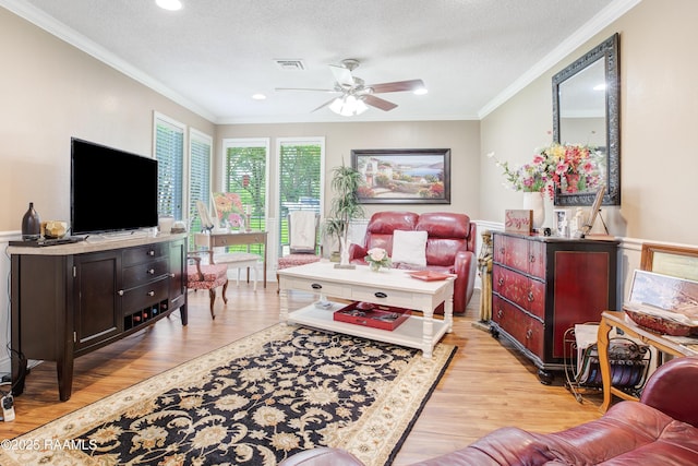 living area with light wood finished floors, a ceiling fan, a textured ceiling, visible vents, and ornamental molding