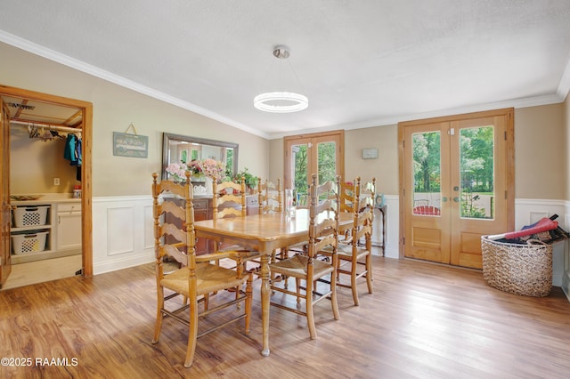 dining room with light wood-style floors, french doors, crown molding, and a wainscoted wall