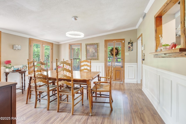 dining area with crown molding, a textured ceiling, light wood-style flooring, and wainscoting