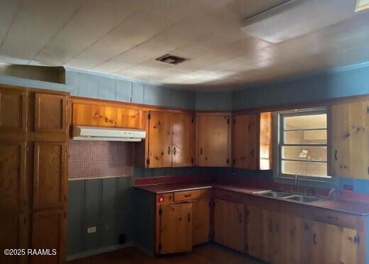 kitchen featuring brown cabinets, a sink, visible vents, and under cabinet range hood