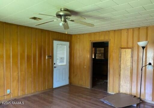 interior space featuring wood walls, visible vents, ceiling fan, and wood finished floors