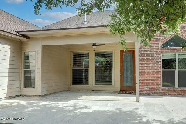 property entrance featuring a patio area, a shingled roof, and brick siding