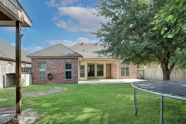 rear view of property featuring a trampoline, brick siding, a patio area, and roof with shingles