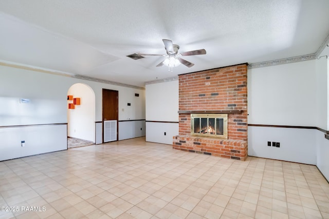 unfurnished living room featuring a brick fireplace, visible vents, a ceiling fan, and arched walkways