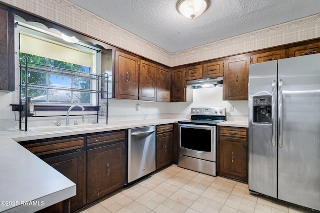 kitchen featuring a sink, a textured ceiling, under cabinet range hood, light countertops, and appliances with stainless steel finishes