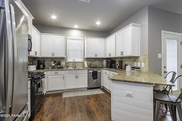 kitchen featuring a sink, a peninsula, black appliances, dark wood finished floors, and white cabinets
