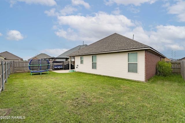 rear view of house featuring a patio, a trampoline, a lawn, a fenced backyard, and roof with shingles