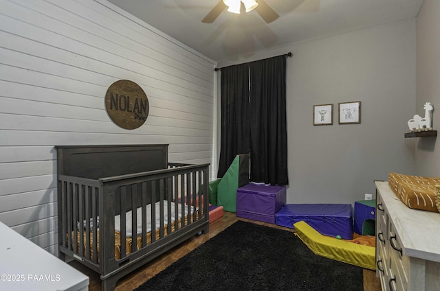 bedroom with a ceiling fan, wooden walls, and wood finished floors