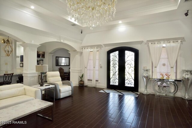 foyer entrance with arched walkways, a chandelier, decorative columns, crown molding, and wood finished floors
