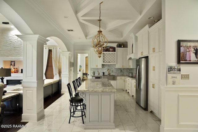 kitchen featuring freestanding refrigerator, light marble finish floors, decorative columns, coffered ceiling, and a kitchen island