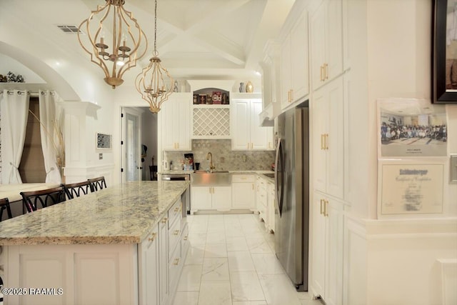 kitchen with freestanding refrigerator, a sink, white cabinetry, light marble finish floors, and a center island