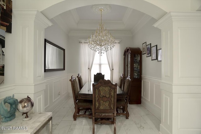dining room with arched walkways, a chandelier, light marble finish flooring, a decorative wall, and a wainscoted wall