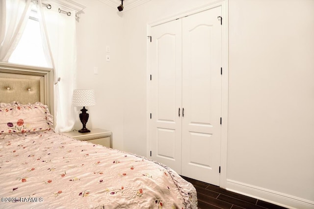 bedroom featuring a closet, crown molding, dark wood-style flooring, and baseboards