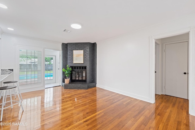 unfurnished living room featuring light wood-style floors, crown molding, and a brick fireplace