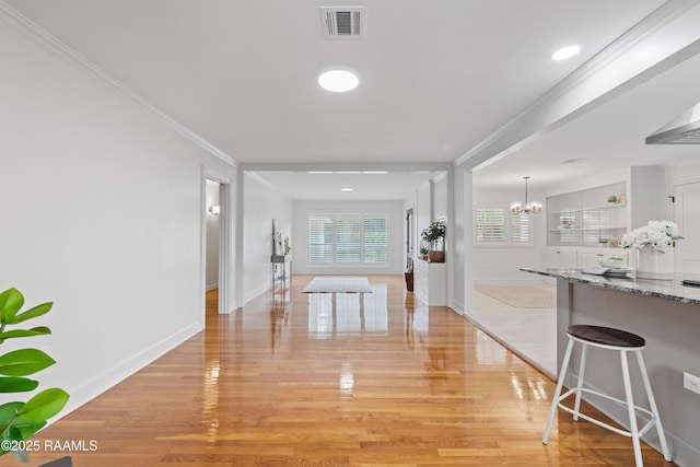 corridor with a chandelier, light wood-type flooring, baseboards, and ornamental molding