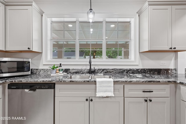 kitchen featuring appliances with stainless steel finishes, a sink, dark stone countertops, hanging light fixtures, and crown molding