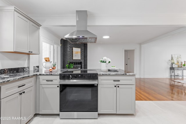 kitchen featuring electric stove, island range hood, a peninsula, light stone countertops, and crown molding