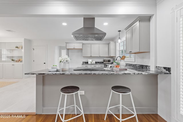 kitchen featuring wall chimney exhaust hood, stone countertops, a peninsula, stainless steel microwave, and light wood-style floors
