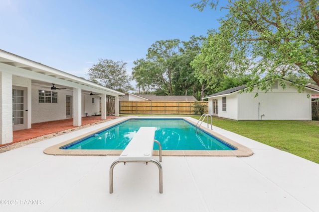 view of swimming pool with ceiling fan, a patio, an outbuilding, and a diving board