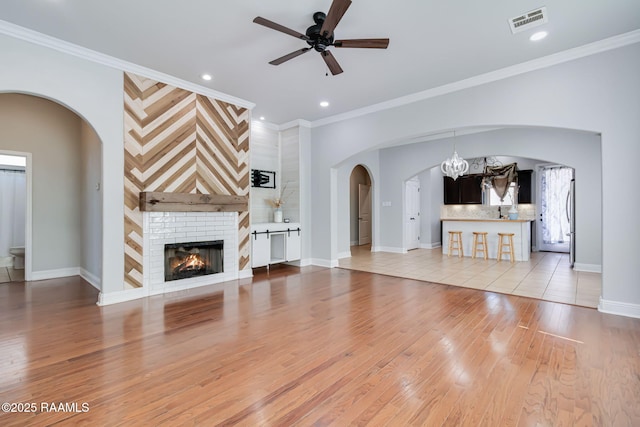 123 Laurel Grove Blvd, Youngsville, LA 70592 - unfurnished living room featuring ceiling fan, arched walkways, light wood-type flooring, a fireplace, and ornamental molding
