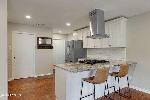 kitchen featuring range hood, freestanding refrigerator, a peninsula, decorative backsplash, and white cabinets