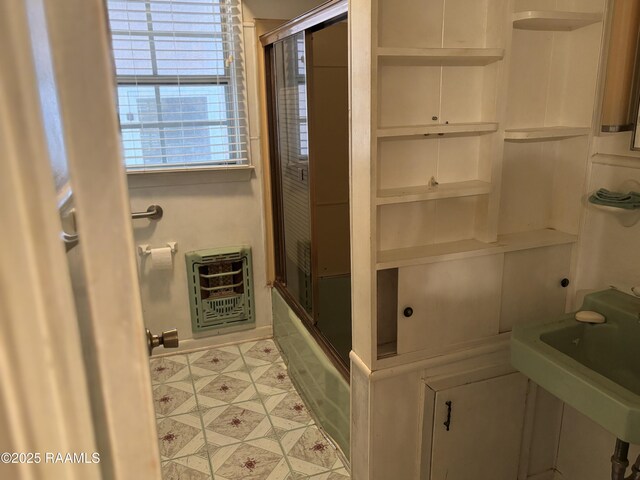 full bathroom with heating unit, enclosed tub / shower combo, a sink, and baseboards