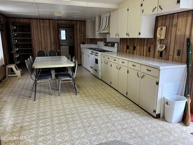 kitchen featuring white gas range, light countertops, wood walls, custom exhaust hood, and light floors