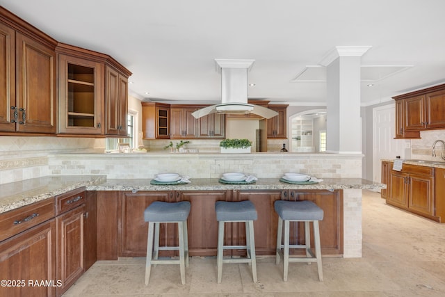 807 Cambridge Dr Res, Unit Res, Lafayette, LA 70503 - kitchen featuring a breakfast bar area, backsplash, glass insert cabinets, light stone counters, and crown molding
