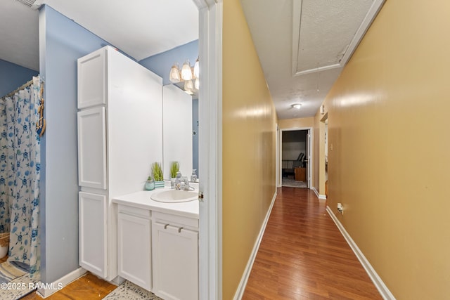 hallway with attic access, a sink, light wood-style flooring, and baseboards