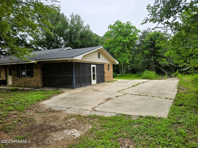 view of side of property featuring a sunroom, brick siding, and a shingled roof