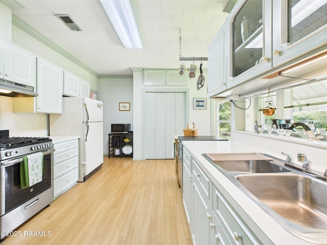 1635 Myrtle Pl, Lafayette, LA 70506 - kitchen with under cabinet range hood, gas range, a sink, light wood finished floors, and white cabinetry