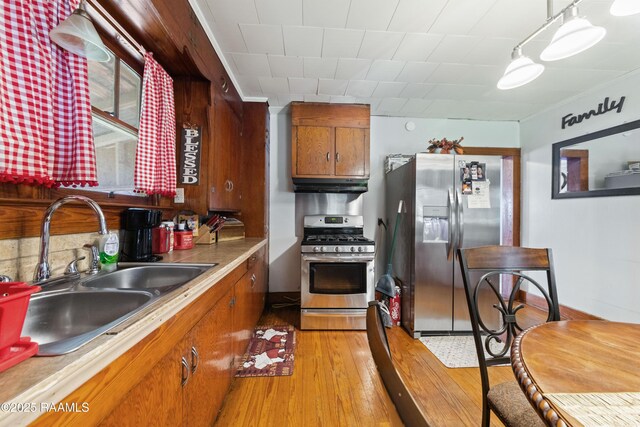 408 Loraine St, Abbeville, LA 70510 - kitchen with appliances with stainless steel finishes, a sink, under cabinet range hood, brown cabinetry, and light wood-type flooring