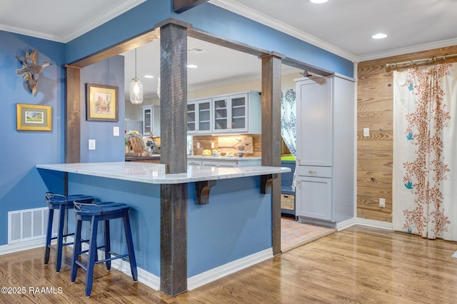 209 Irene Cir, Lafayette, LA 70503 - kitchen with decorative columns, a kitchen bar, light wood-type flooring, light stone countertops, and crown molding