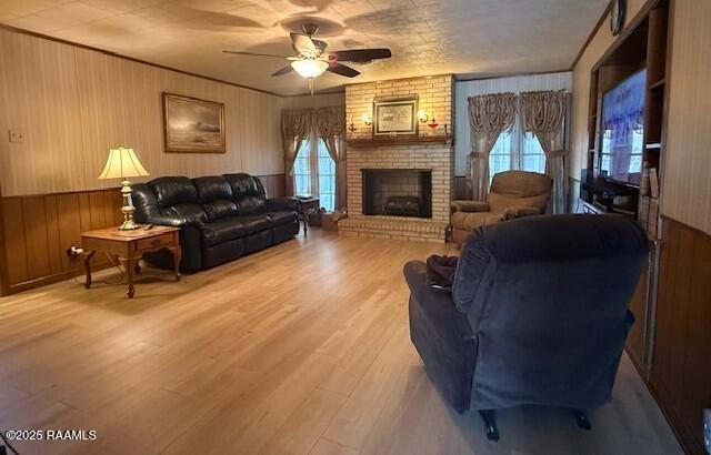 living room featuring ceiling fan, a fireplace, wooden walls, and wood finished floors