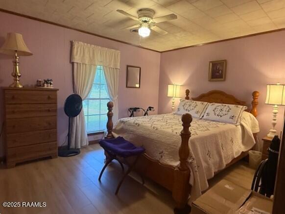 bedroom with wood finished floors, crown molding, and ceiling fan