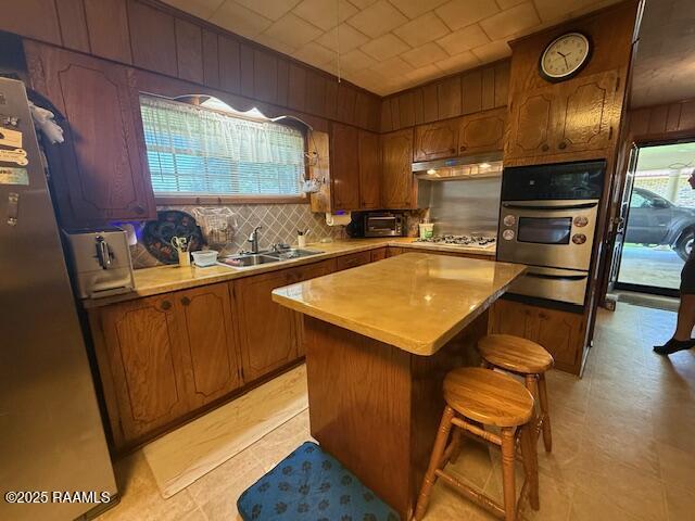 kitchen with stainless steel appliances, a sink, a warming drawer, plenty of natural light, and wood walls