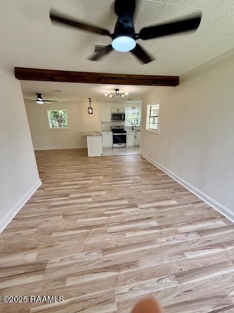 unfurnished living room featuring a ceiling fan, healthy amount of natural light, light wood finished floors, baseboards, and beamed ceiling