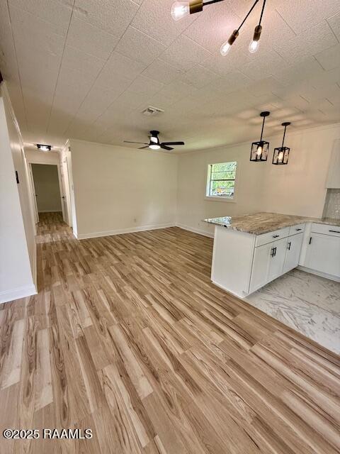 unfurnished living room featuring light wood-style flooring, ceiling fan, and baseboards