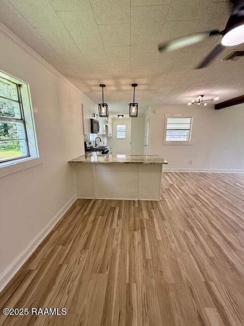 kitchen featuring a peninsula, ornamental molding, light wood-style flooring, white cabinets, and hanging light fixtures