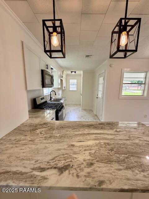 kitchen featuring appliances with stainless steel finishes, a sink, white cabinetry, light stone counters, and pendant lighting