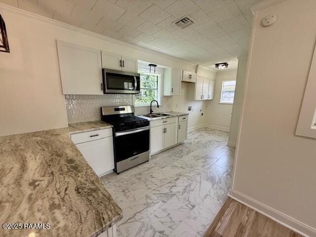 kitchen with appliances with stainless steel finishes, a sink, ornamental molding, light stone counters, and white cabinetry