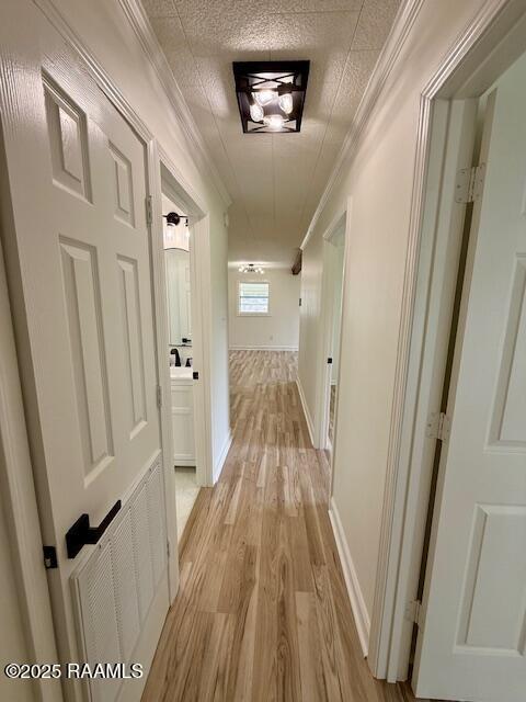 hallway with light wood-style floors, ornamental molding, an ornate ceiling, and baseboards
