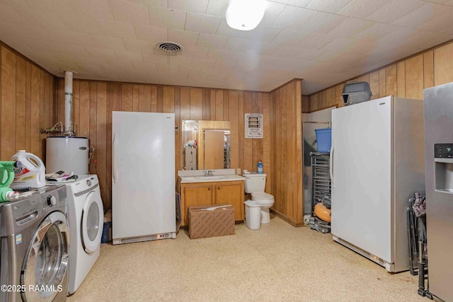 1005 Tensas Dr, Opelousas, LA 70570 - laundry area with gas water heater, washing machine and clothes dryer, wood walls, a sink, and light floors