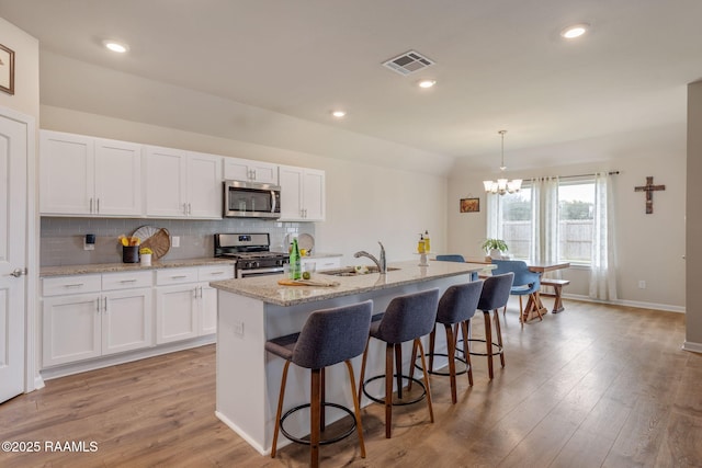 110 Casa Bella Ct, Breaux Bridge, LA 70517 - kitchen with appliances with stainless steel finishes, a chandelier, white cabinetry, backsplash, and a kitchen bar