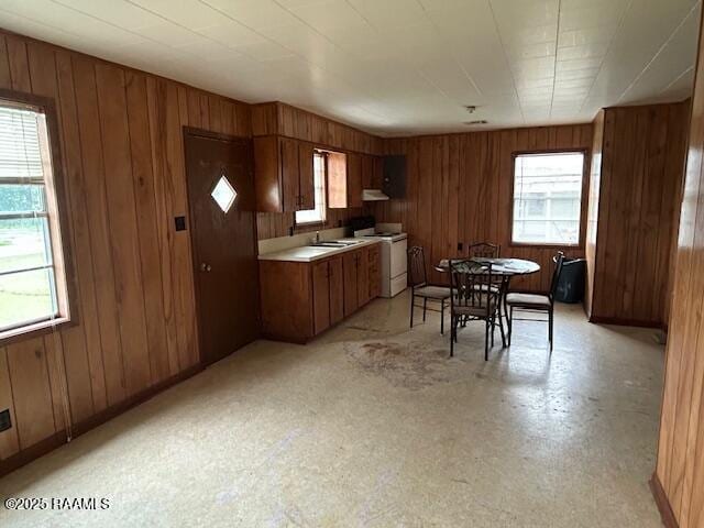 143 Monette St, Ville Platte, LA 70586 - kitchen with white electric range, brown cabinetry, wood walls, light countertops, and under cabinet range hood