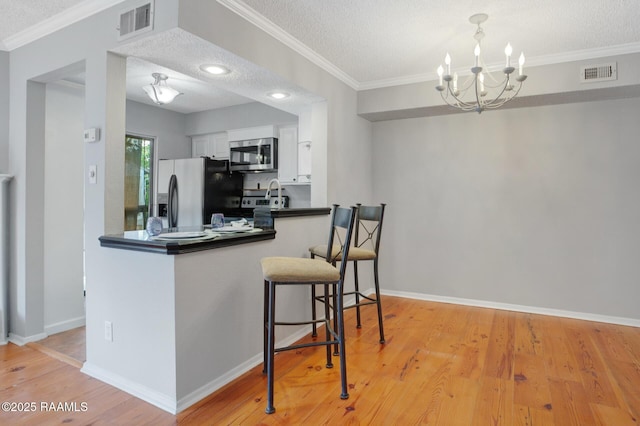 1304 E Bayou Pkwy Unit 4A, Lafayette, LA 70508 - kitchen featuring stainless steel appliances, white cabinets, a chandelier, a textured ceiling, and light wood-type flooring