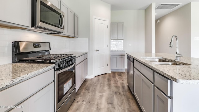316 White Pine Dr, Lafayette, LA 70501 - kitchen featuring stainless steel appliances, a sink, gray cabinets, light wood-style floors, and light stone counters