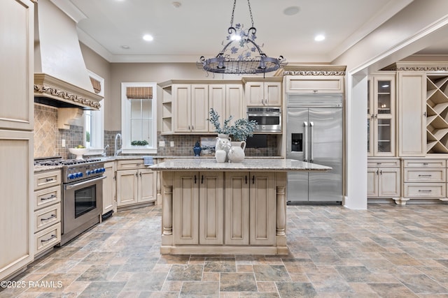 104 Avallach Dr, Lafayette, LA 70503 - kitchen with premium appliances, wall chimney range hood, cream cabinets, open shelves, and a center island