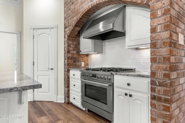 40400 Abby James Rd, Prairieville, LA 70769 - kitchen featuring stainless steel gas range oven, wall chimney exhaust hood, dark wood-style flooring, white cabinetry, and light stone countertops