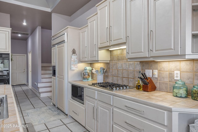 102 Capilano Ln, Broussard, LA 70518 - kitchen featuring built in appliances, tile countertops, light tile patterned floors, backsplash, and white cabinets